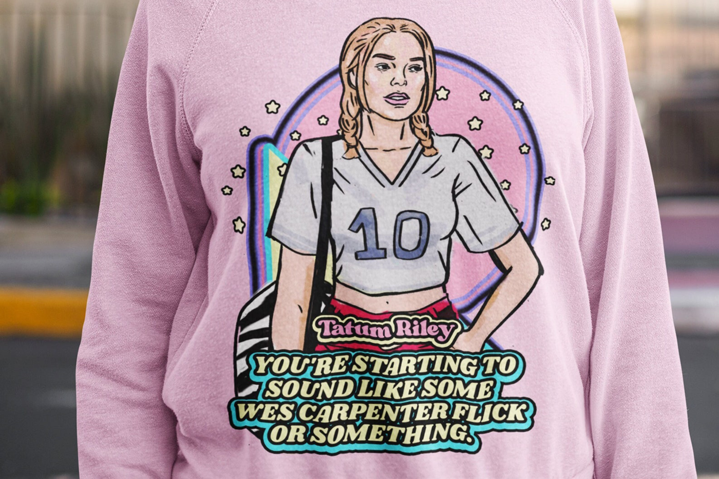 Closeup photo of female model wearing pastel pink crew neck sweatshirt with retro illustration of Tatum Riley (Rose McGowan) from Scream (1996) with movie quote below